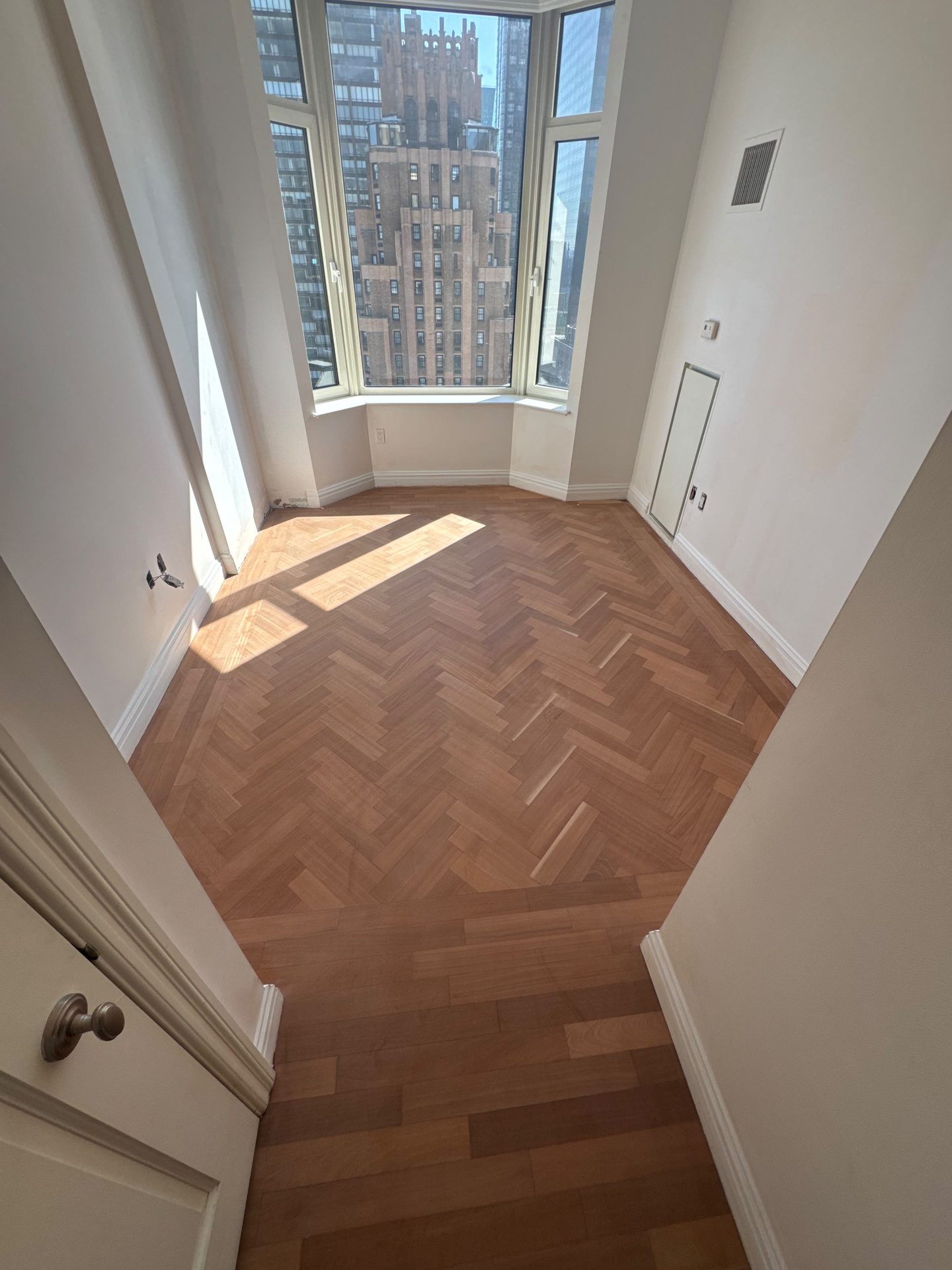 Herringbone floor beneath a bay window with skyline beyond